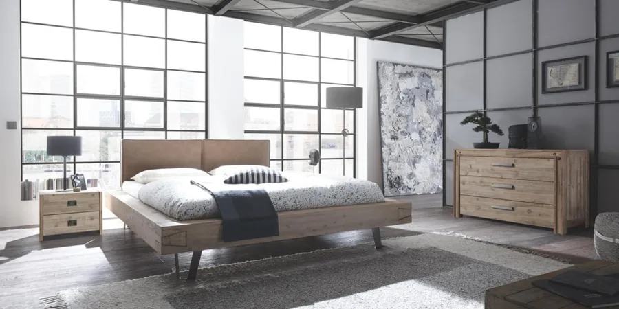 Loft-Schlafzimmer mit Holzbett, Kommode und großen Sprossenfenstern.