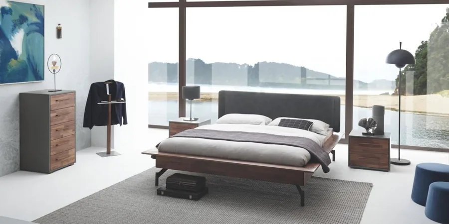 Schlafzimmer mit Holzbett, Nachttischen, Herrendiener und großer Fensterfront mit Seeblick.