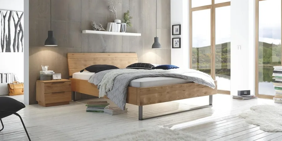 Helles Schlafzimmer mit Eichenbett auf Metallkufen, Nachttisch und Wandregal.