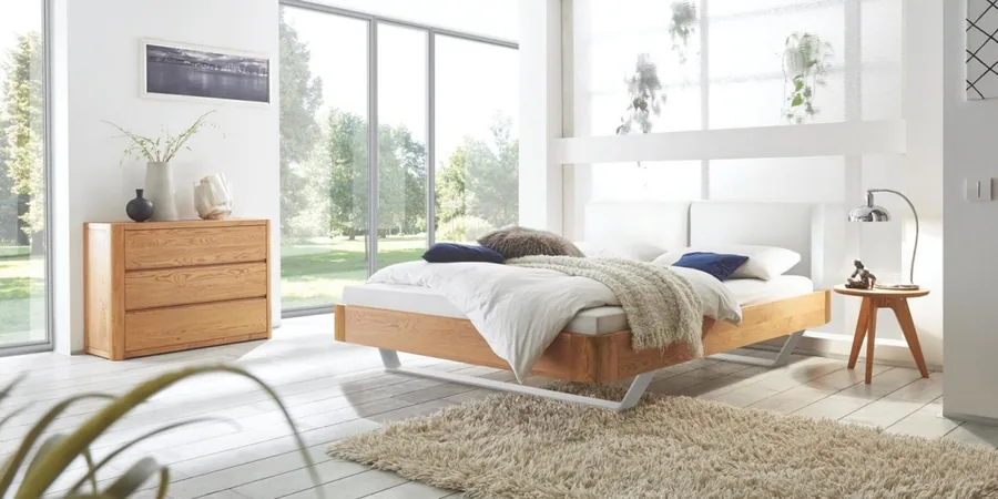 Schlafzimmer mit Eichenbett, Kommode, Teppich und bodentiefen Fenstern mit Blick ins Grüne.