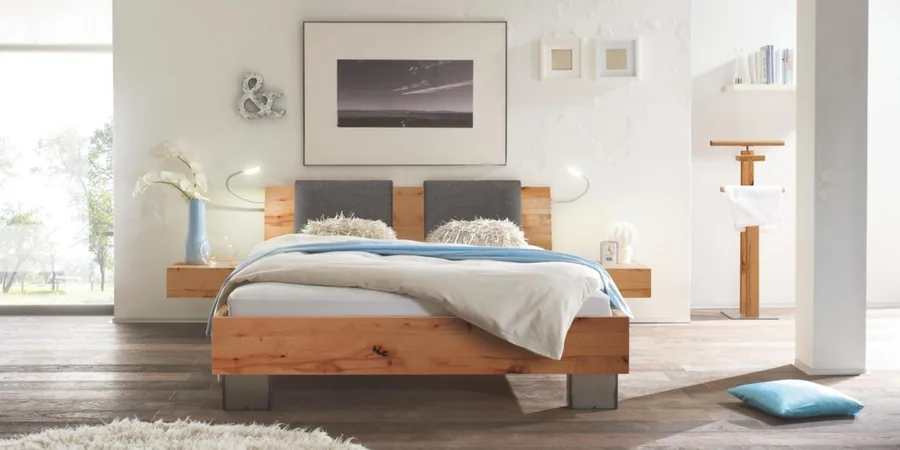 Helles Schlafzimmer mit niedrigem Holzbett, grauem Kopfteil und Bild an der Wand.