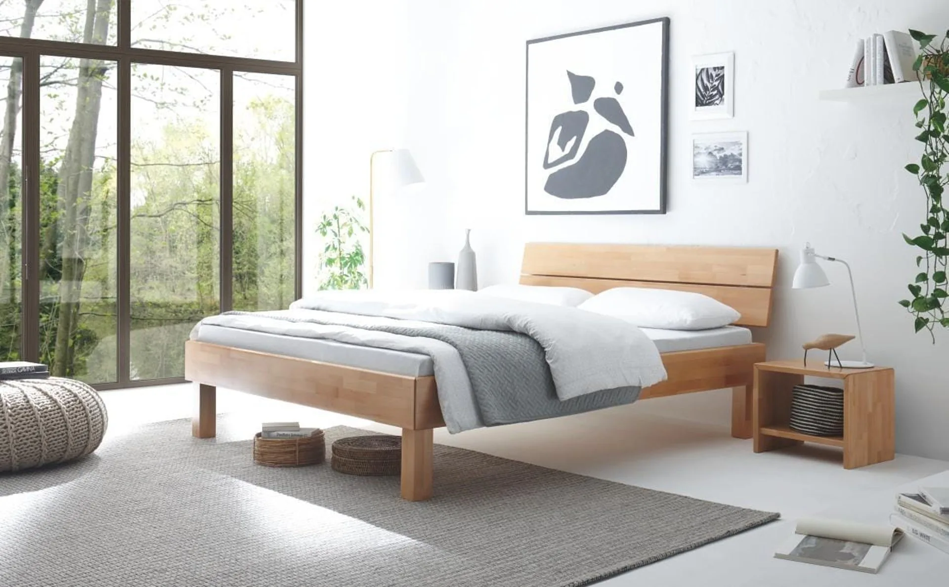 Helles Schlafzimmer mit massivem Holzbett, Nachttisch und großem Fenster mit Blick ins Grüne.