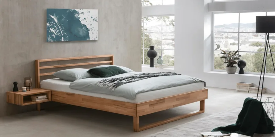 Schlafzimmer mit hellem Holzbett, grauer Bettwäsche und einem blauen Bild über dem Kopfteil.