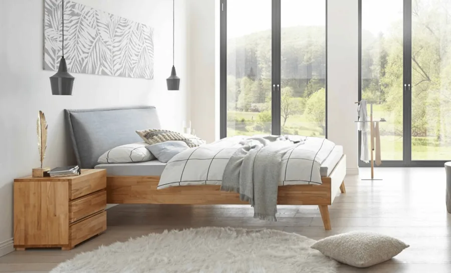 Helles Schlafzimmer mit Holzbett, karierter Bettwäsche und Pendelleuchten vor bodentiefen Fenstern.