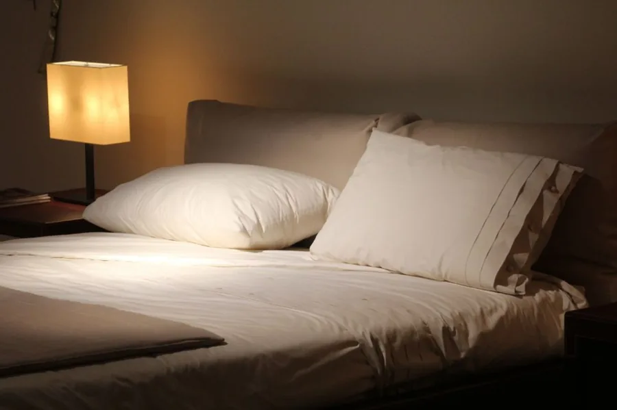 Warm beleuchtetes Schlafzimmer mit aufgeschlagenem Bett, weißen Kissen und Nachttischlampe.